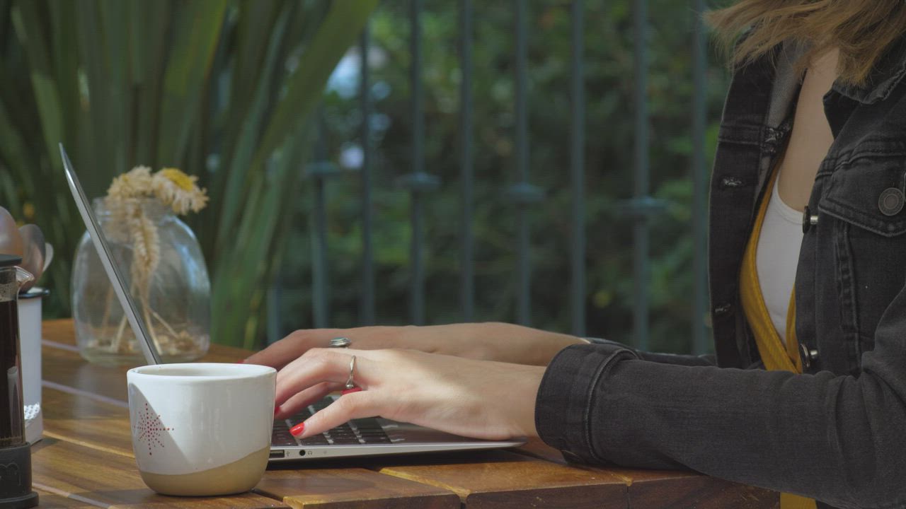 Someone working on a laptop at an outdoor table, a cup of coffee beside them